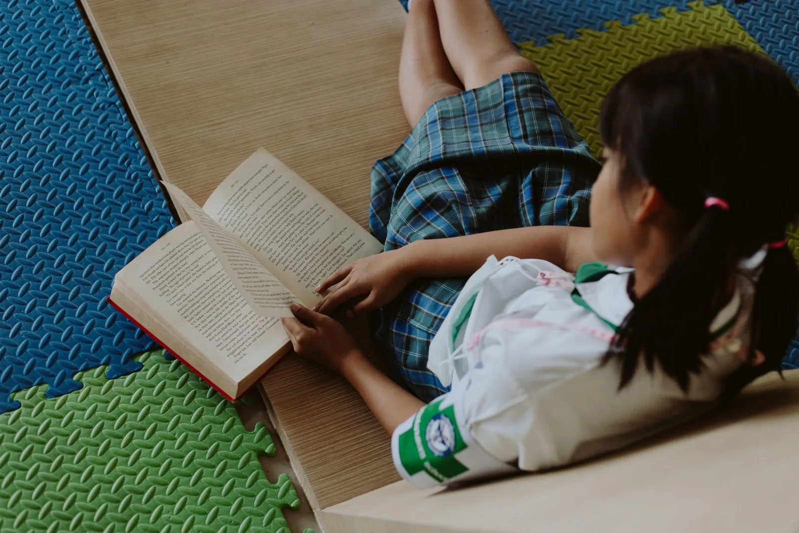 Niña leyendo un libro sentada sobre un piso de goma de colores