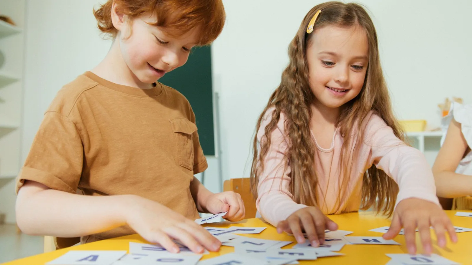 Niño y niña juegan a ordenar tarjetas con letras sobre una mesa amarilla