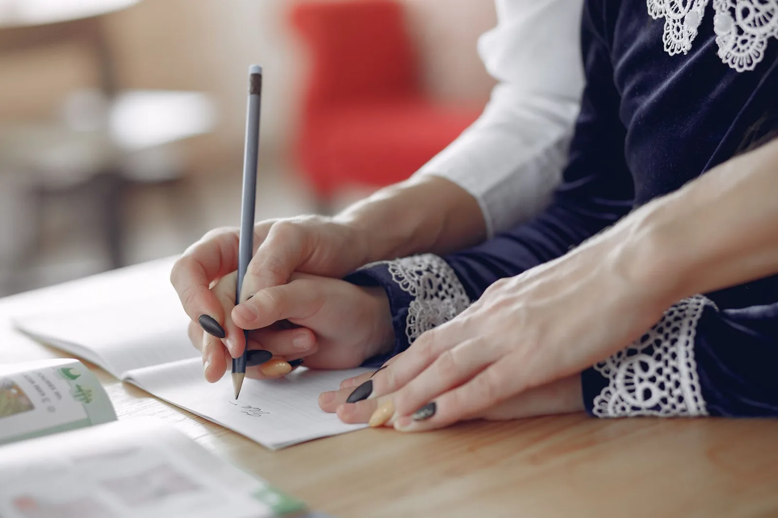 Mano de una adulta guía la mano de una niña que escribe en su cuaderno